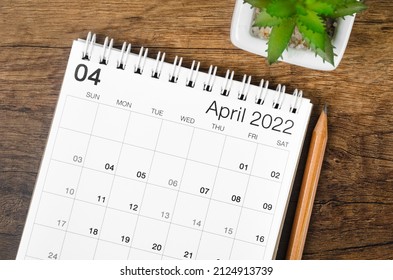The April 2022 desk calendar with plant on wooden table.