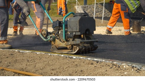 APRIL 2022, LJUBLJANA, SLOVENIA: Construction Worker Using Vibration Compactor For Laying Asphalt Surface At Yard. Working Men In Beautiful Morning Light. Men In Uniform Asphalt Paving The Driveway.