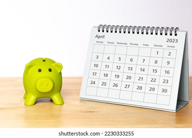 April 2023 calendar - monthly page and little piggy bank on a wooden table