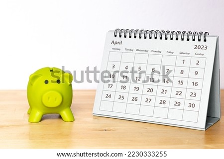 April 2023 calendar - monthly page and little piggy bank on a wooden table Imagine de stoc © 