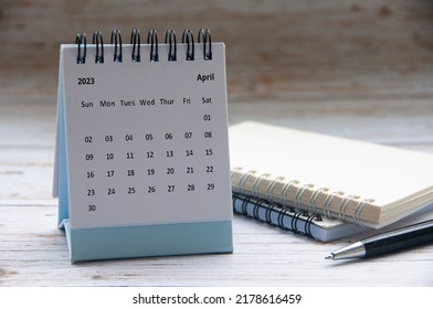 April 2023 white desk calendar on wooden table with notepad and pen background. New year concept and copy space