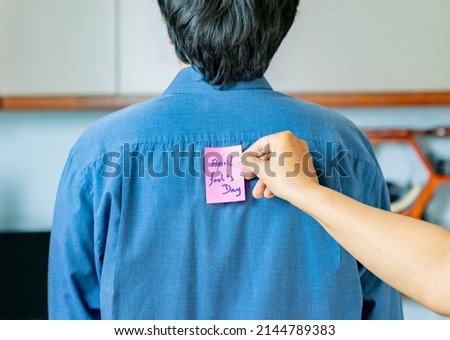 April fools day concept. A woman putting note with april fools day lettering on males back.