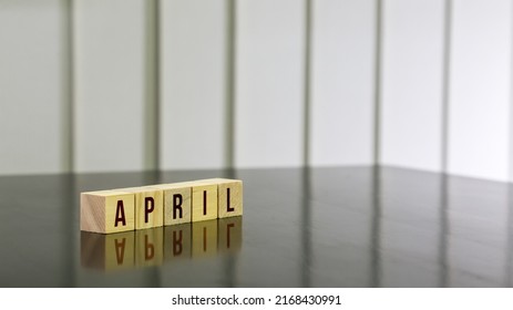 APRIL Word On Wooden Cube On Black Gloss Wooden Table. Selected Focus