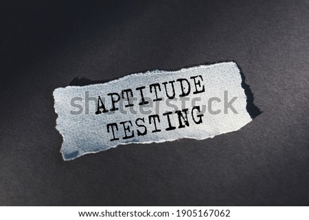 APTITUDE TESTING - text on torn paper on dark desk in sunlight.