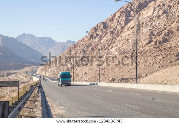 Aqaba highway in a stone desert and trucks on\
the road , Jordan\
