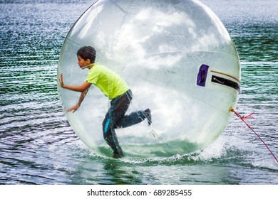 Aquazorbing activity with a child running inside a transparent inflatable ball on water, representing fun, outdoor entertainment, summer recreation and active leisure on the lake.