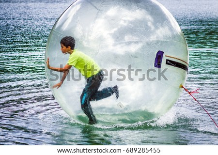 Aquazorbing activity with a child running inside a transparent inflatable ball on water, representing fun, outdoor entertainment, summer recreation and active leisure on the lake.