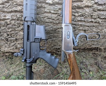 An AR15 Style Assault Rifle And A Vintage Lever Action Rifle Leaning Up Against A Log.