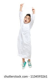 Arab boy jumping high with a big smile and open eyes, wearing white traditional Saudi Thobe and sneakers, on white isolated background