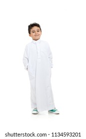 Arab boy relaxed and smiling, wearing white traditional Saudi Thobe and sneakers, raising his hands on white isolated background