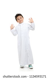 Arab boy smiling, wearing white traditional Saudi Thobe and sneakers, raising his hands on white isolated background