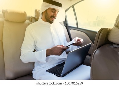 Arab Business Man With Mobile Phone And Laptop Reading Market Trends, News, Online Banking Or Purchasing Online