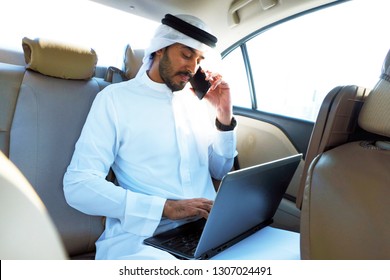 Arab Business Man Talking To A Bank Representative While Performing Online Banking Through His Electronic Devices - Mobile Phone And Laptop