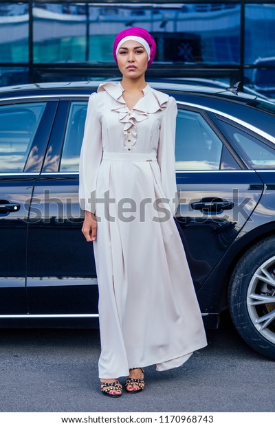 Arab business woman hijab\
standing in front of her luxury car on the street on a background\
of skyscrapers of Dubai. The woman is dressed in a stylish\
abaya