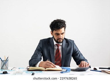 Arab Businessman Calculating Budget At Office Desk. Financial Expertise And Consulting. Manager In Suit And Tie Sitting At Desk With Documents And Calculator. Corporate Accounting And Paperwork