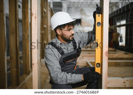 Arab construction worker using spirit level ensuring vertical alignment of wooden beam during modular house construction in a workshop