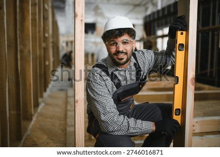 Arab construction worker using a spirit level ensures the precise vertical alignment of a wooden beam within a prefabricated house structure