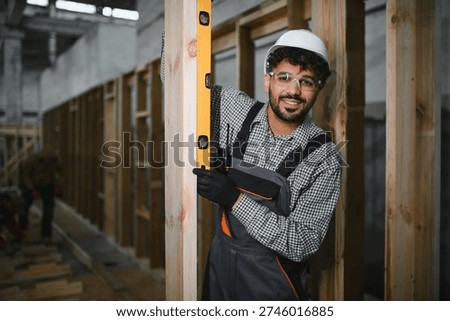 Arab construction worker using a spirit level ensures precise vertical alignment of wooden beams in a modular house production workshop