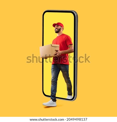 Arab Courier Guy Coming Out Of Big Phone Screen Carrying Parcel Box Delivering Package Over Yellow Studio Background. Delivery Service, Mobile App For Your Smartphone. Square Shot