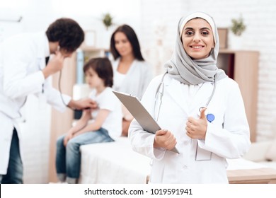 An Arab Doctor In Hijab Poses With A History Of The Disease In His Hands. Arabian Hospital Concept. Pediatrician Office And Sick Child.