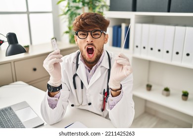 Arab Doctor Man With Beard Holding Covid Test Angry And Mad Screaming Frustrated And Furious, Shouting With Anger. Rage And Aggressive Concept. 