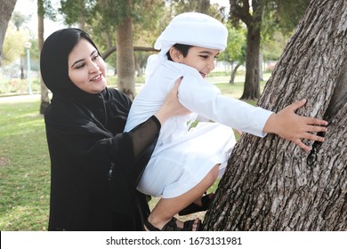 Arab Emirati Mother At Day Time With Arabic Son. UAE Mom On Abaya Spending Time With Boy Child At A Park. Arabian Kid Climbing On A Tree