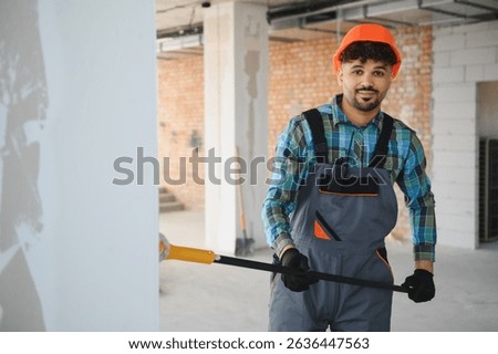 Arab engineer removing plaster from a wall using a scraper tool, working on a renovation project in a building under construction