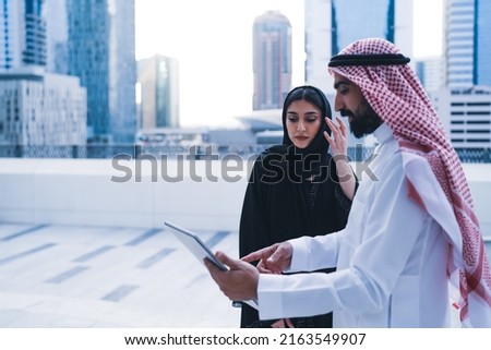 Arab family or colleagues working on laptop or tablet showing looking in business background wearing traditional abaya and dress. Muslim Saudi or Arabian people teamwork success.