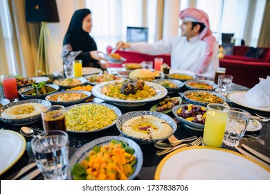 Arab Family In Traditional Clothes Eating During The Holy Month Of Ramadan At Iftar. Feast In Honor Of Eid Mubarak.The Family Sits On The Background Of A Table Filled With Traditional Food,Eid Al Adha