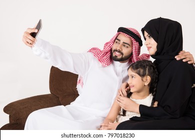 Arab Family Using Smart Phone And Taking Selfie While Sitting On Sofa Chair At Home With White Background