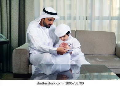 Arab father helping son with his homeschool activities. Arabic child with this daddy wearing traditional kandura