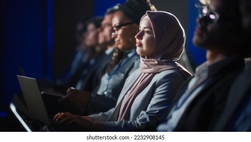 Arab Female Sitting in a Dark Crowded Auditorium at a Human Rights Conference. Young Muslim Woman Using Laptop Computer. Activist in Hijab Listening to Inspiring Speech About Global Initiative. - Powered by Shutterstock