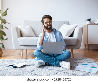 Arab Freelancer Guy Using Laptop And Talking On Cellphone At Home, Smiling Eastern Man In Eyeglasses Working Remotely With Computer And Documents While Sitting On Floor In Living Room, Copy Space