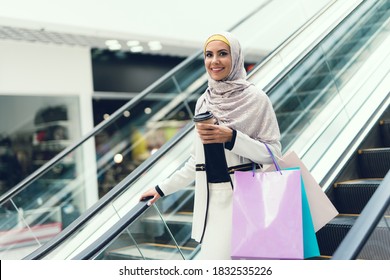 Arab girl with a cup of coffee rides on an escalator and looks at the camera. Young girl in arab clothes with a cup of coffee in hand. - Powered by Shutterstock