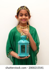 Arab girl dressed up for Eid festival wearing a traditional arabic green dress with gold ear ring, head and neck jewellery and holding a lantern in hand.