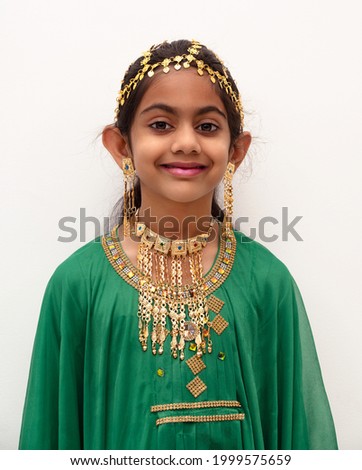 Arab girl dressed up for Eid festival wearing a traditional arabic green dress with gold ear ring, head and neck jewellery.