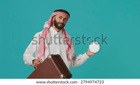 Arab guy sees wall clock to check time on camera, using timepiece to look at hour and minutes, with young person in traditional Muslim clothing examining local timezone, standing over background.