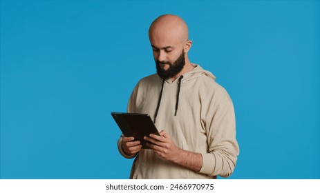 Arab guy using tablet to scroll on online websites, looking for something on the internet and using social media apps. Modern person working with touchscreen device in studio. Camera 1. - Powered by Shutterstock - Get 15% off with code: PIKWIZARD15