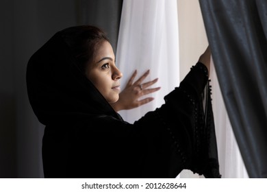 An arab lady wearing Abaya the traditional dress looking out through a window
