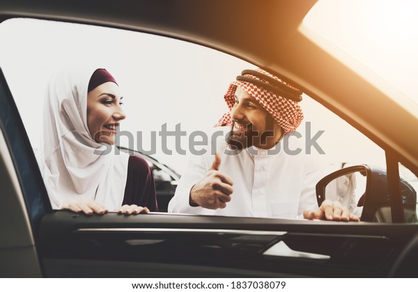 Arab looks at his wife and shows a gesture\
super. Arab woman in hijab looks at the man with whom he chooses a\
new car at a car\
dealership.