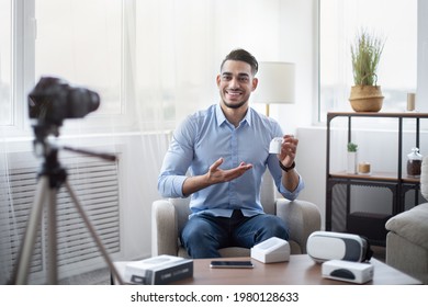 Arab male blogger promoting new model of wireless earphones, filming video review of modern gadget at home. Famous influencer making content for his tech channel, recommending innovative product