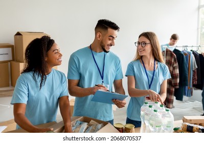 Arab Male Manager Checking Donation List And Writing In Clipboard. Diverse Volunteer Workers Working In Shipping Delivery Charitable Stock Organization Packing Donations Boxes