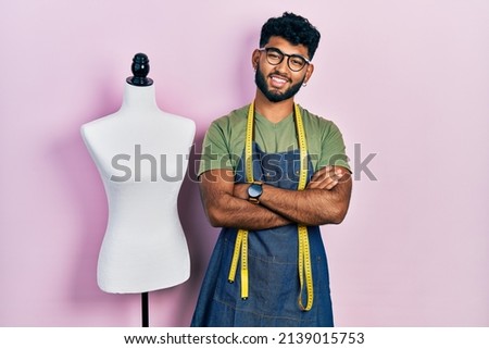 Arab man with beard dressmaker designer wearing atelier apron smiling with a happy and cool smile on face. showing teeth. 