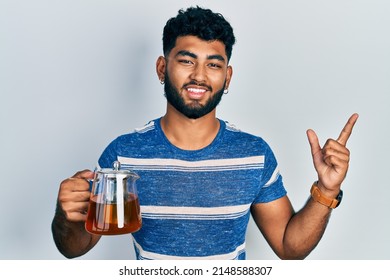 Arab Man With Beard Holding Traditional Tea Pot Smiling Happy Pointing With Hand And Finger To The Side 