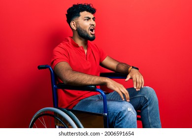 Arab man with beard sitting on wheelchair angry and mad screaming frustrated and furious, shouting with anger. rage and aggressive concept. 