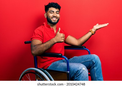Arab man with beard sitting on wheelchair showing palm hand and doing ok gesture with thumbs up, smiling happy and cheerful 