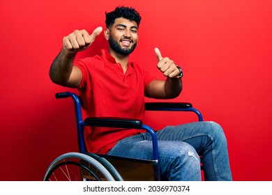 Arab man with beard sitting on wheelchair approving doing positive gesture with hand, thumbs up smiling and happy for success. winner gesture. 