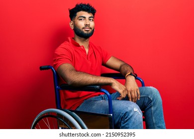 Arab man with beard sitting on wheelchair smiling looking to the side and staring away thinking. 