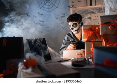 Arab Man Business Owner Wears White Clay Skull, Professional Makeup In Home Office. Accepts An Order On The Site Writes The Address On The Box. Festive Decorated Office. Halloween Sale Concept