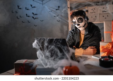 Arab Man Business Owner Wears White Clay Skull, Professional Makeup In Home Office With Headset. Sitting Bored. Festive Decorated Office. Halloween Sale Concept. Banner. Copy Space.